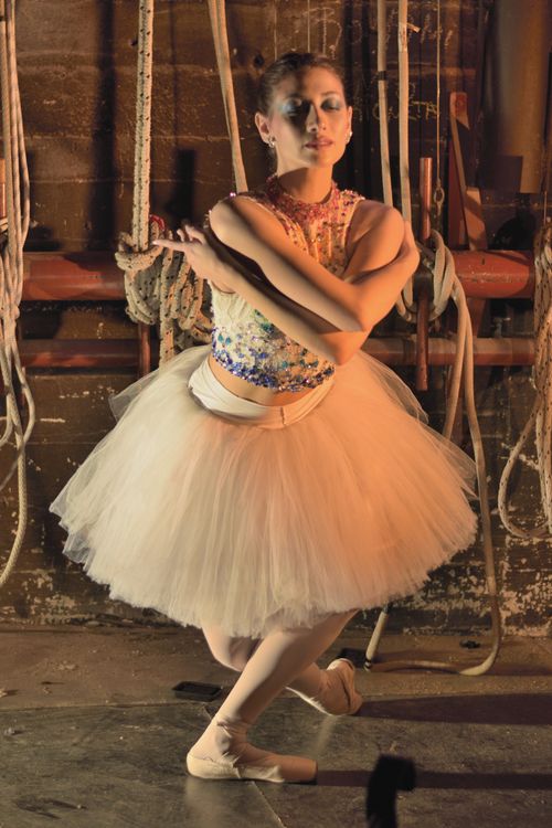 Free Graceful ballerina in a tutu poses elegantly with dramatic lighting in a dance studio. Stock Photo