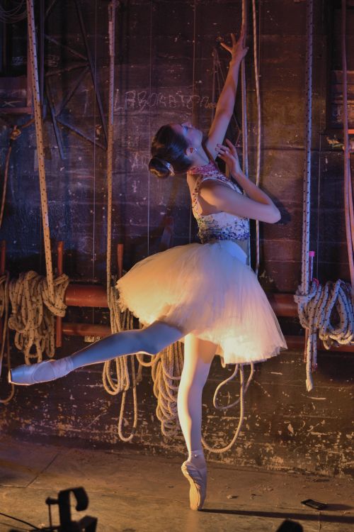 Free Ballet dancer poised elegantly on tiptoe in a dimly lit backstage setting of a theater. Stock Photo