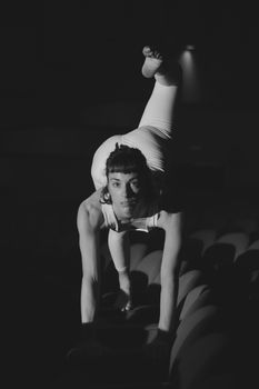 Artistic monochrome photo of a woman stretching in a theater setting.