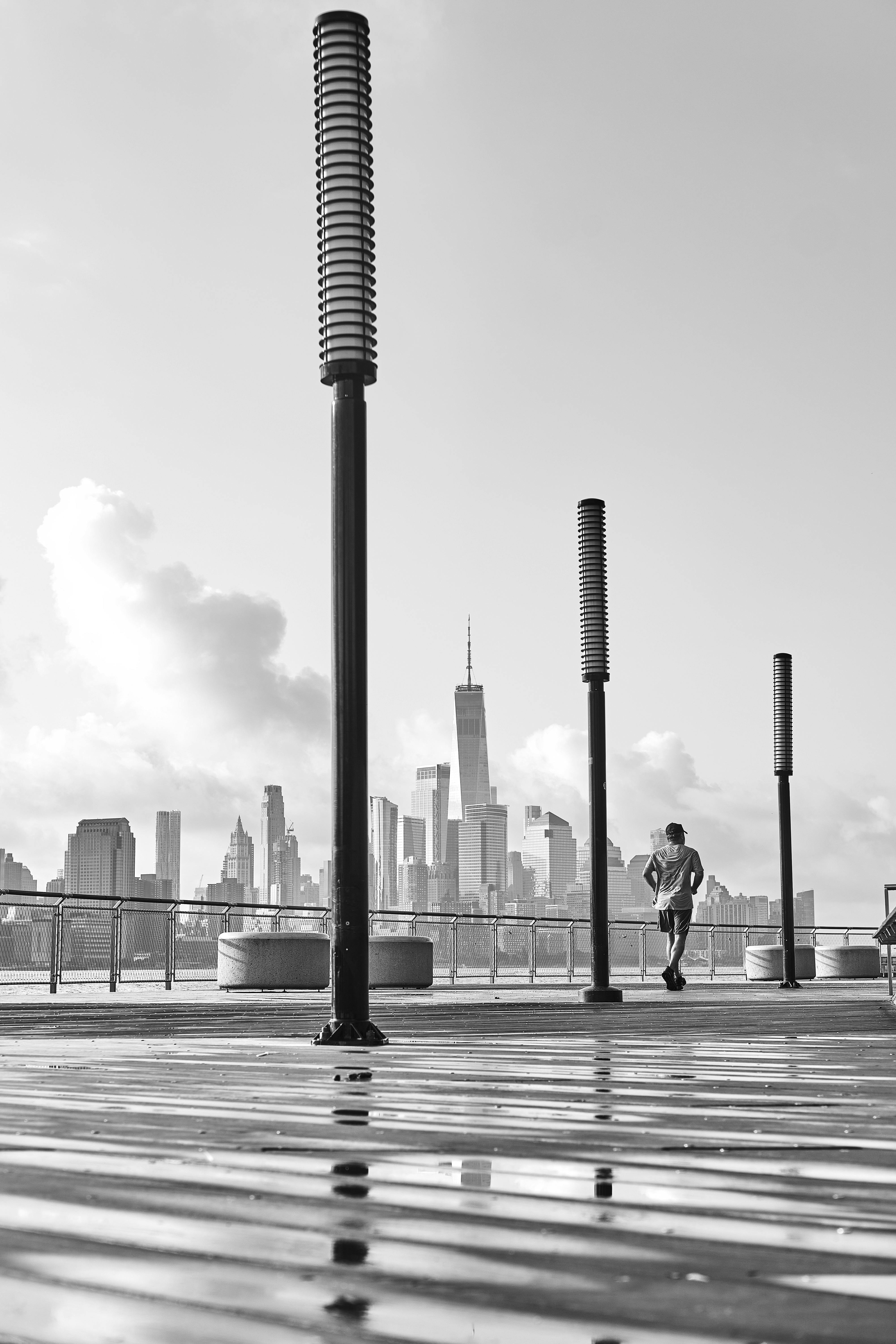 Black and white shot of a city skyline viewed from a waterfront boardwalk with modern lamp posts.