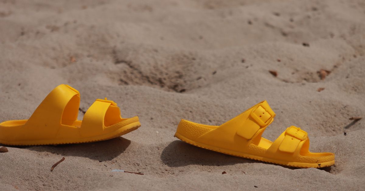 Close-up of yellow sandals resting on sandy beach in Alghero, Sardinia, Italy.