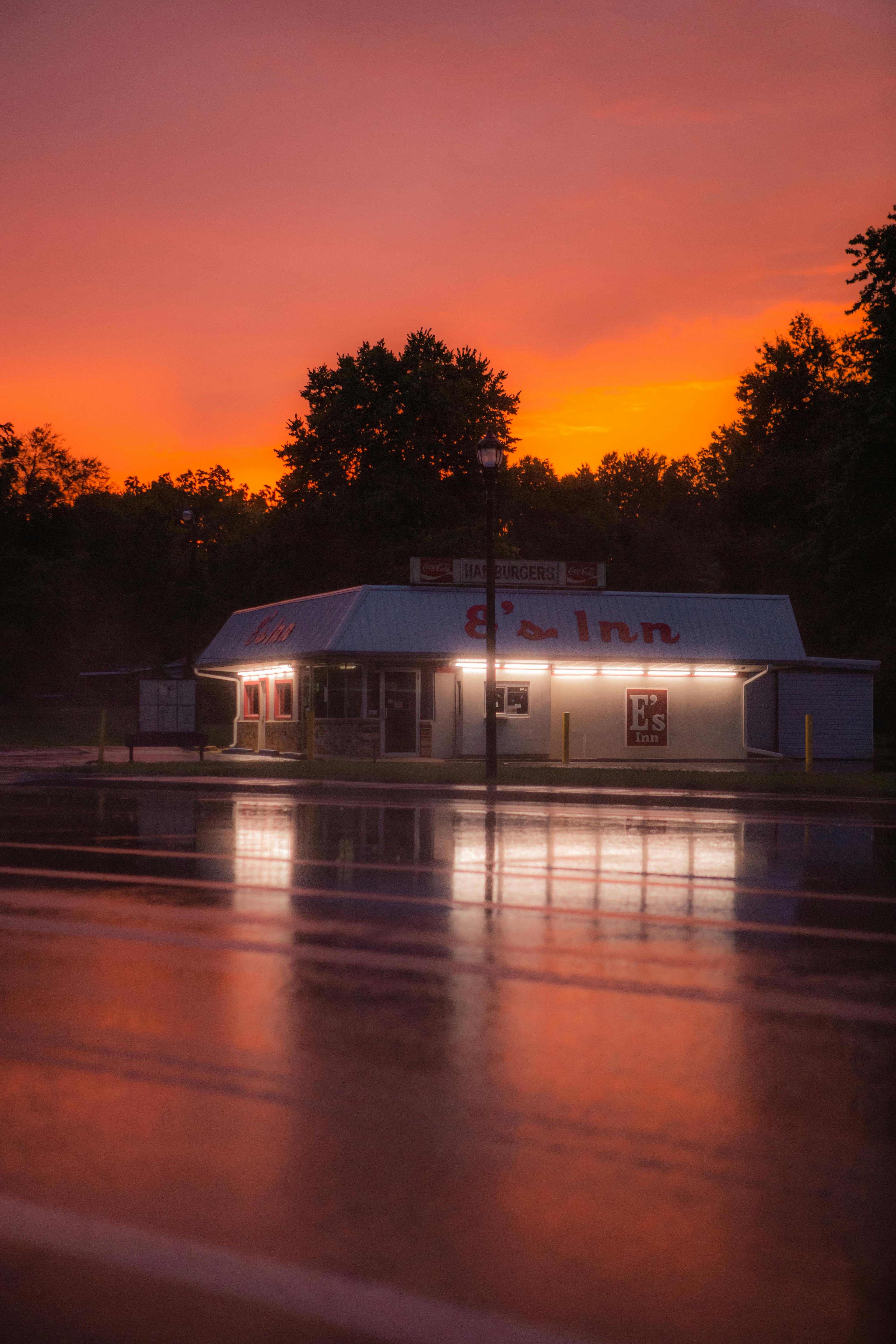 Charming roadside inn with vibrant sunset sky reflecting on wet pavement, capturing serene evening ambiance.