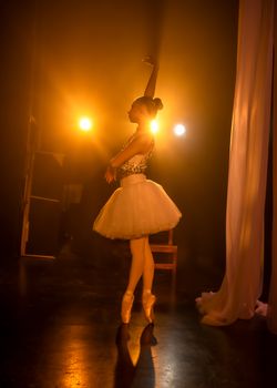 Graceful ballerina performing under dramatic spotlight in theater setting.