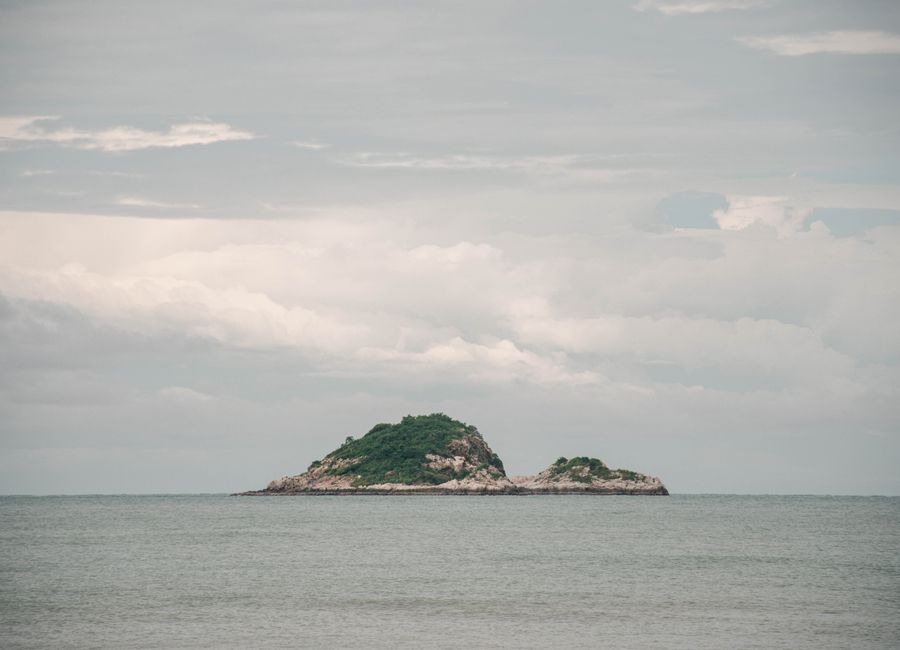 Serene view of a small island surrounded by the sea and cloudy sky in Hua Hin, Thailand.