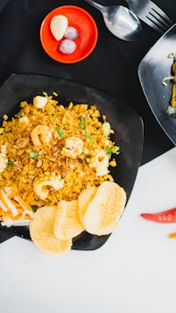 Tasty plate of Indonesian fried rice with prawns and crackers, garnished with fresh vegetables.