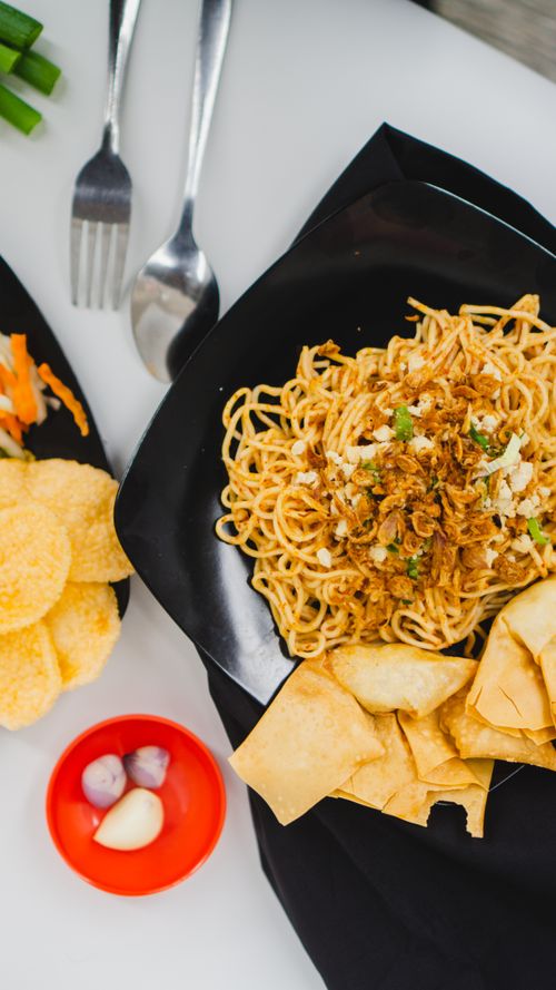 Free Appetizing Asian noodles dish with crispy toppings, served on a black plate for a gourmet presentation. Stock Photo