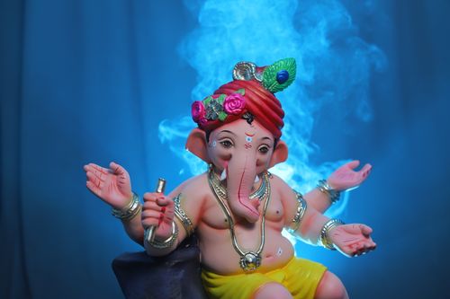 Free A vibrant Ganesha statuette adorned with jewelry against a mystical blue smoke background. Stock Photo
