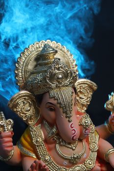 Close-up of a detailed Ganesha statue with a vibrant blue smoky background, symbolizing Hindu spirituality.