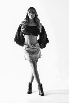 Black and white studio shot of a fashionable woman posing in a denim skirt and crop top.
