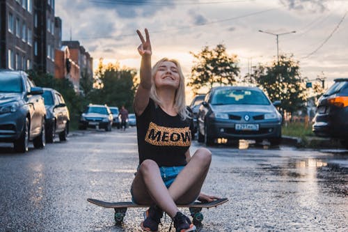免费 打手势和平标志时坐在滑板上的女人 素材图片