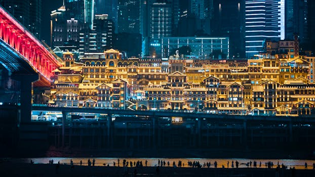 Stunning aerial view of a cityscape with illuminated buildings and vibrant bridge at night, showcasing architectural beauty.