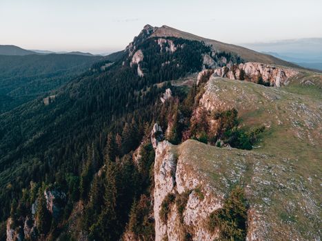Breathtaking aerial photo of a rugged mountain range in Romania, showcasing lush greenery and dramatic cliffs.