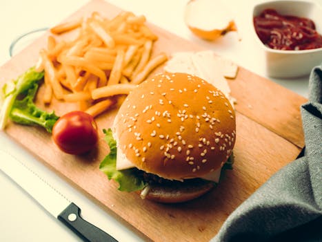 A delicious burger served with french fries and garnishes on a wooden cutting board.