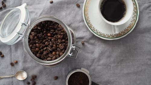Free Top view of a coffee setup featuring a cup of black coffee, coffee beans, and a saucer on a fabric mat. Stock Photo