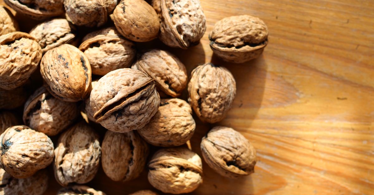 A detailed close-up of whole walnuts placed on a wooden table in bright lighting.