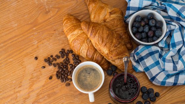 A tasty breakfast setup featuring croissants, coffee, blueberries, and jam.