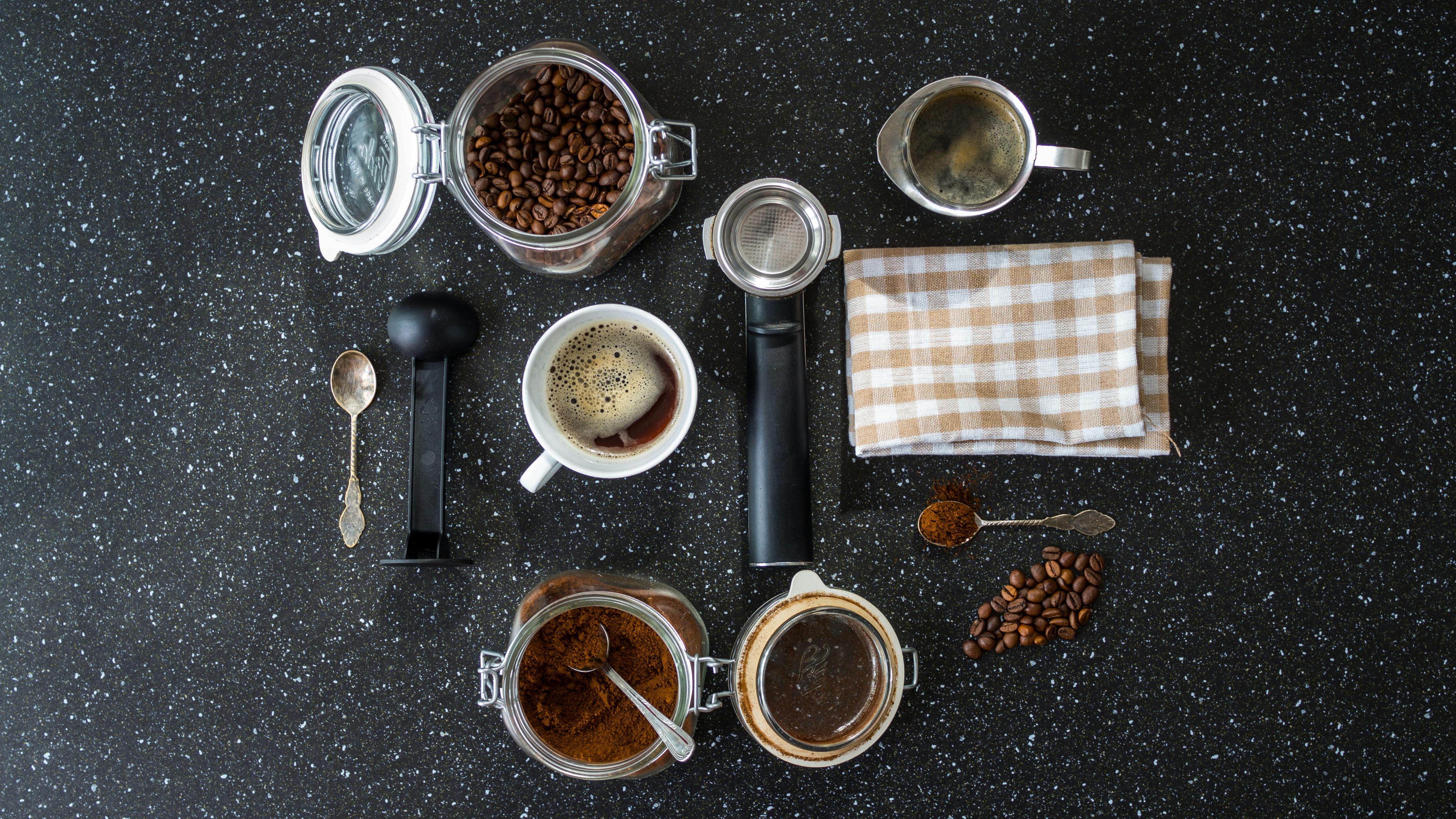 Vue plongeante sur un setup café avec grains, tasse et accessoires sur granit noir