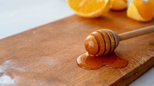 Free Close-up of a honey dipper on a wooden board with oranges, showcasing natural food photography. Stock Photo