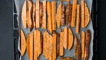 Seasoned raw sweet potato wedges lined up on a parchment baking tray before roasting