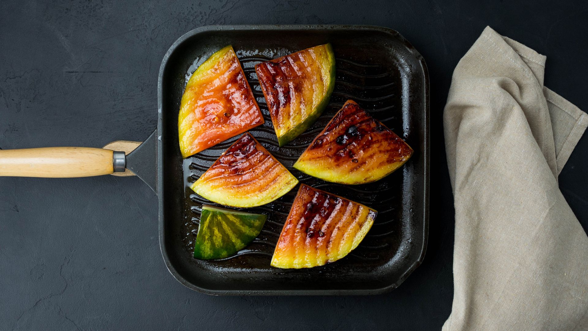 Juicy grilled watermelon slices on a non-stick pan with a napkin beside it.