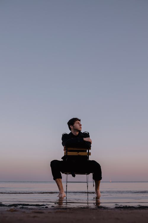Man Sitting Backwards on Chair on a Sandy Beach 