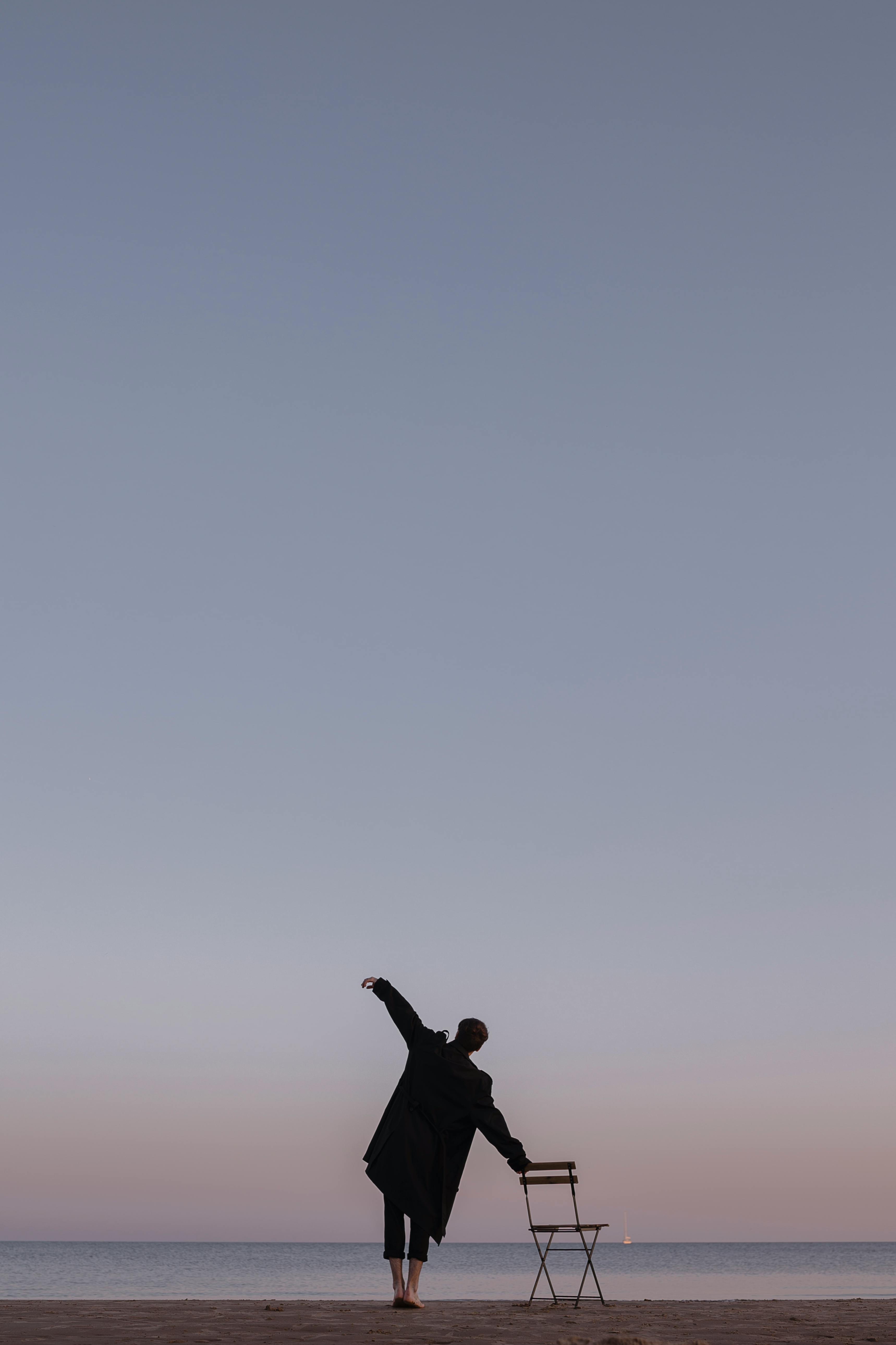 一名男子赤脚站在海滩上，用椅子在风景如画的日落天空中保持平衡