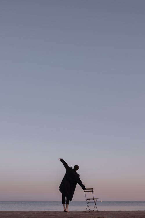 Man Standing Barefoot on the Beach and Leaning on the Chair 