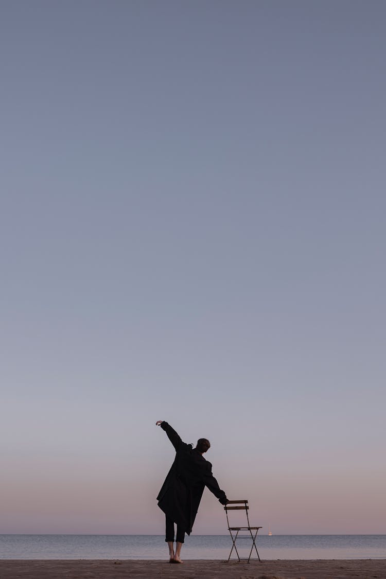 Man Standing Barefoot On The Beach And Leaning On The Chair 