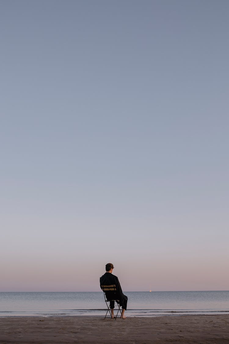 Man Sitting On Chair On The Beach And Looking At Sea 