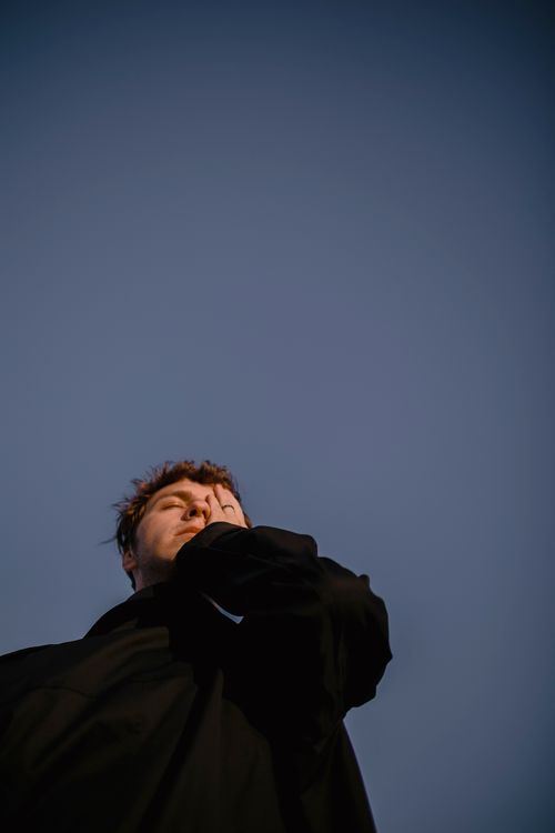 Free A dramatic low-angle shot of a man in a black coat against a clear sky, conveying a moody atmosphere. Stock Photo