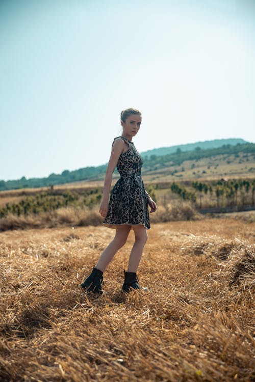 Girl in Sleeveless Dress and Black Boots Walking on Brown Grass