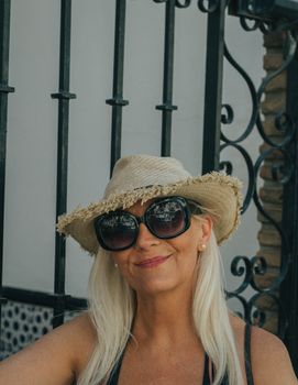 Casual portrait of a smiling woman wearing sunglasses and a straw hat in sunny Mijas, Spain
