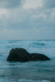 Capture of dynamic ocean waves crashing onto a rock under a cloudy sky in Jawa Barat, Indonesia.