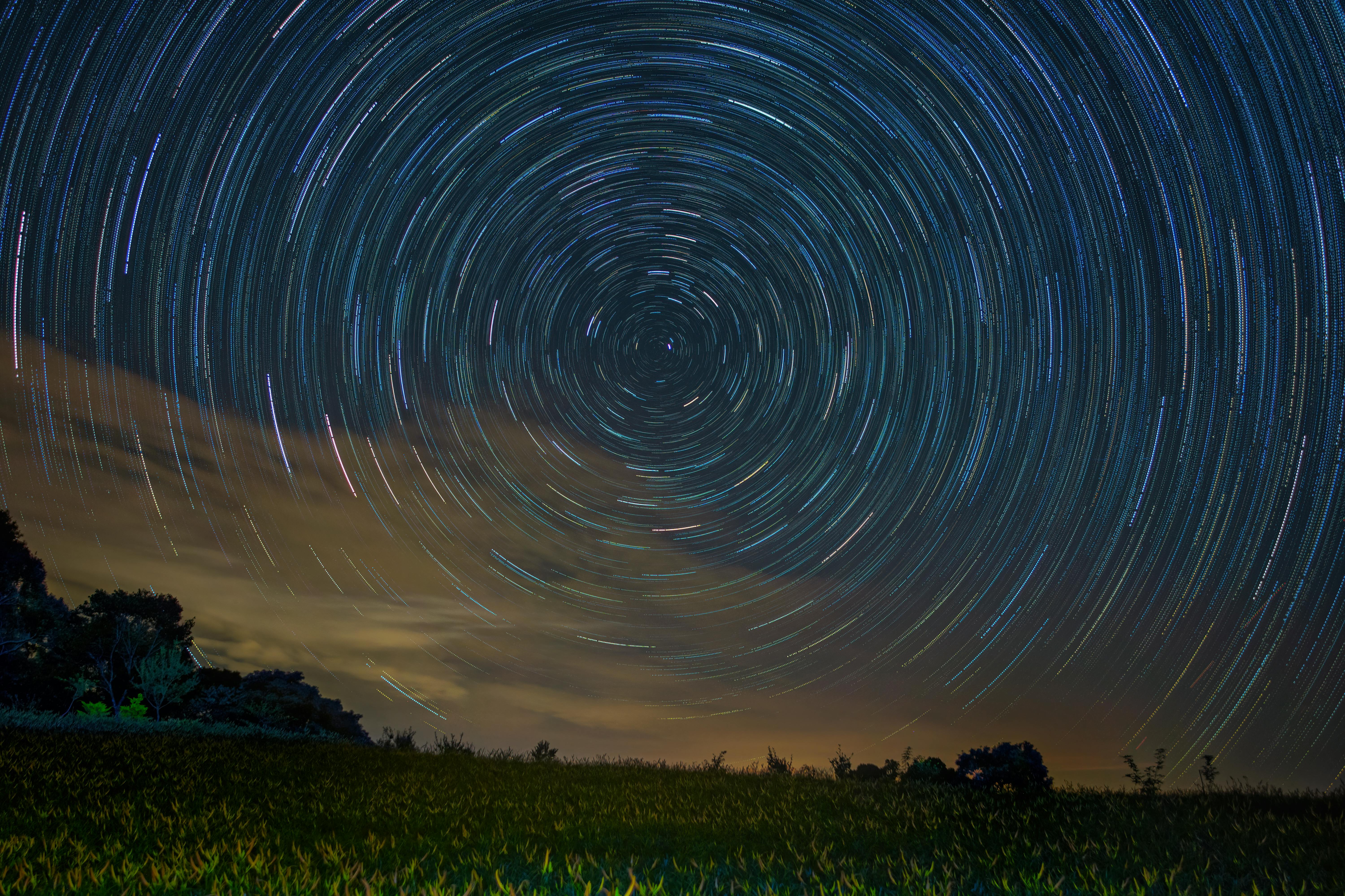 Majestic night sky with swirling star trails captured over a serene meadow.
