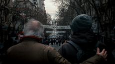 Crowds gather at a street demonstration in Buenos Aires, Argentina, with historic architecture in the background.