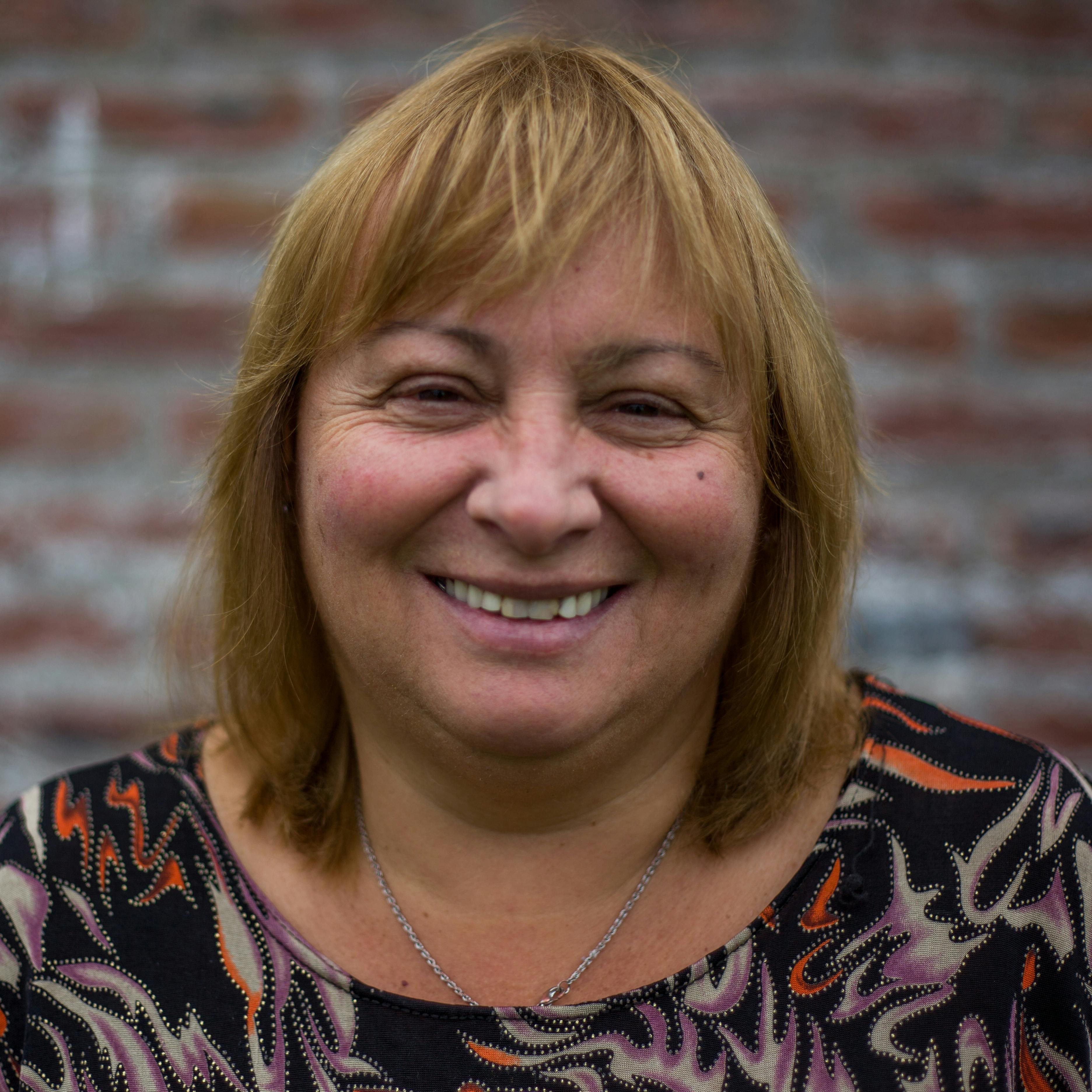 Close-up portrait of a smiling woman against a brick wall in Mar del Plata, Argentina.