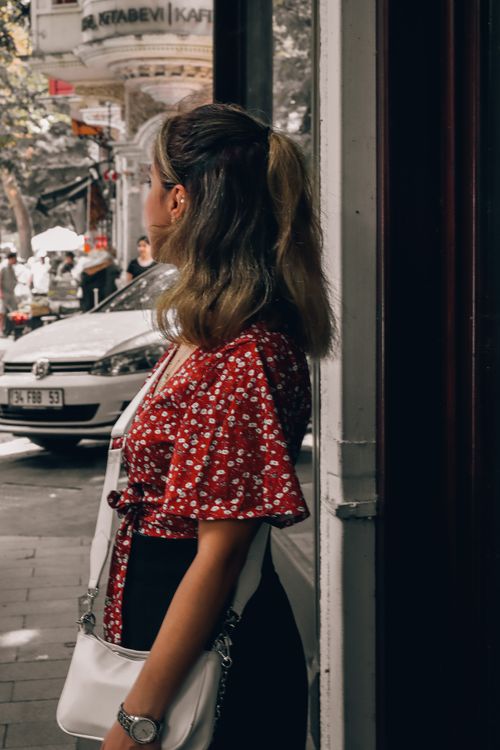 Free Brunette woman in floral dress gazing down urban street on a sunny day. Stock Photo