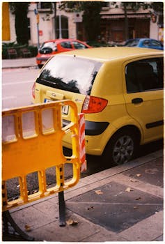 A yellow car parked on a Barcelona street beside a safety barrier, capturing urban life.