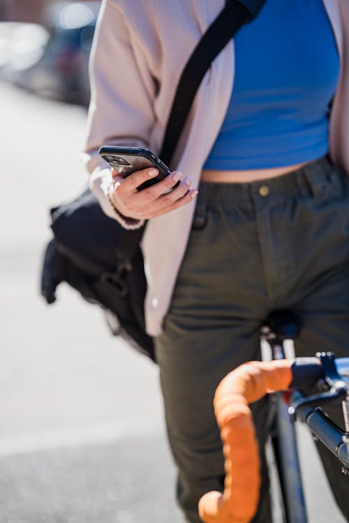 Unrecognizable Woman Sitting on Bike and Holding Mobile Phone