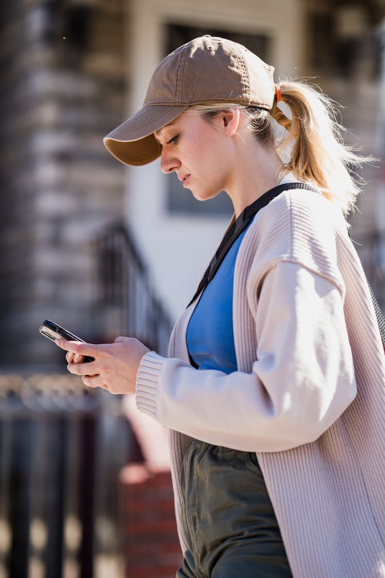 Blonde Girl In Cap Texting On Mobile Phone