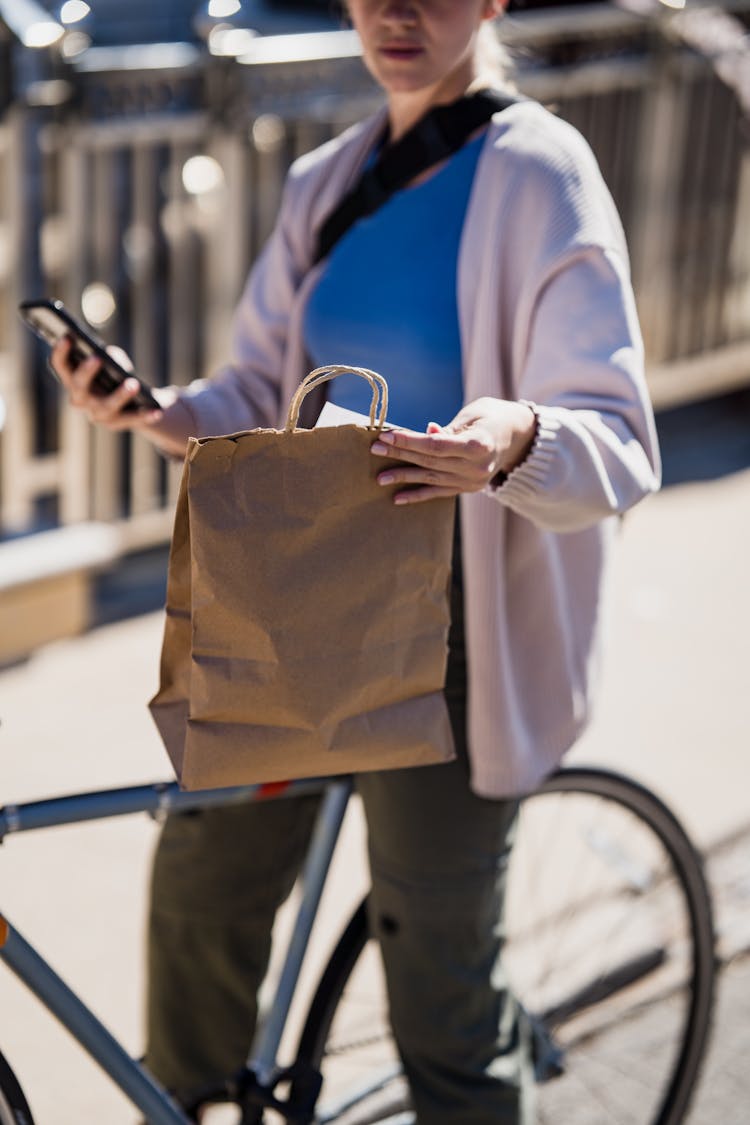 Delivery Woman Sitting On Bike And Looking At Paper Bag