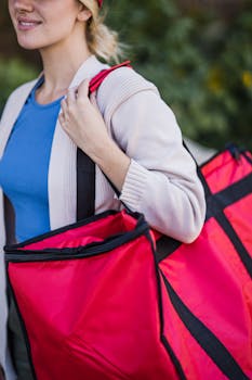 Portrait of a young woman carrying a large delivery bag outdoors.