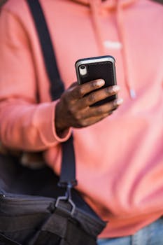 Close-up of a man in a pink hoodie using a smartphone outdoors, highlighting casual technology use.
