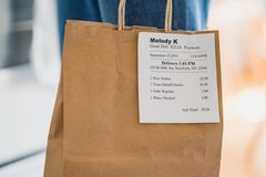 Close-up of a brown paper bag with a receipt for a food service order, held indoors.