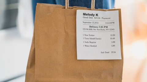 Close-up of a brown paper bag with a receipt for a food service order, held indoors.