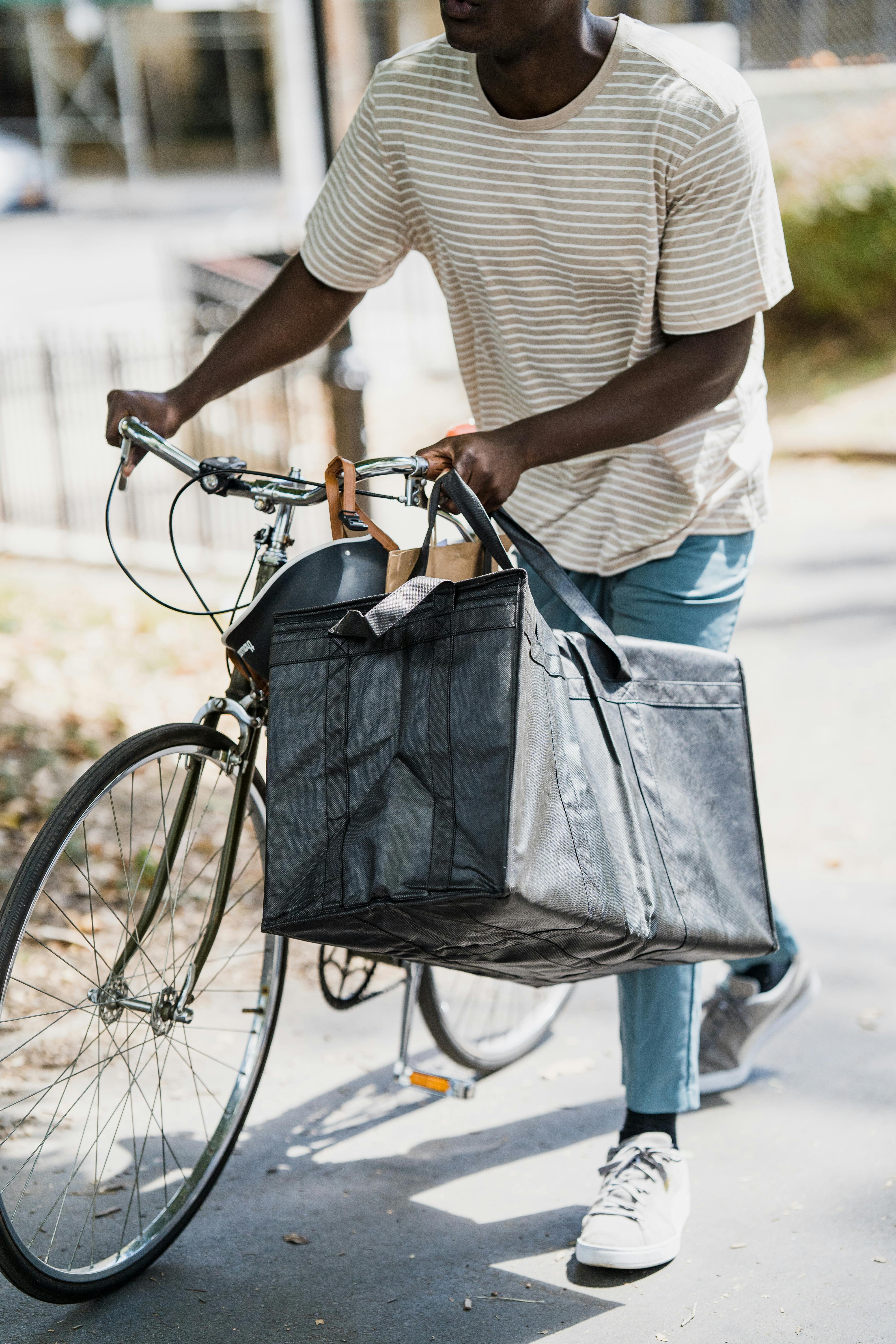 young man working as a food delivery man carrying a food delivery bag and pushing a bicycle