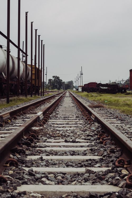 Free Perspective view of railroad tracks leading to an industrial area with cloudy skies. Stock Photo