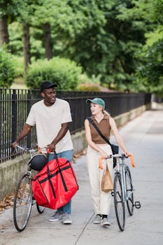 Two cyclists with delivery bags talking while walking on a city sidewalk.