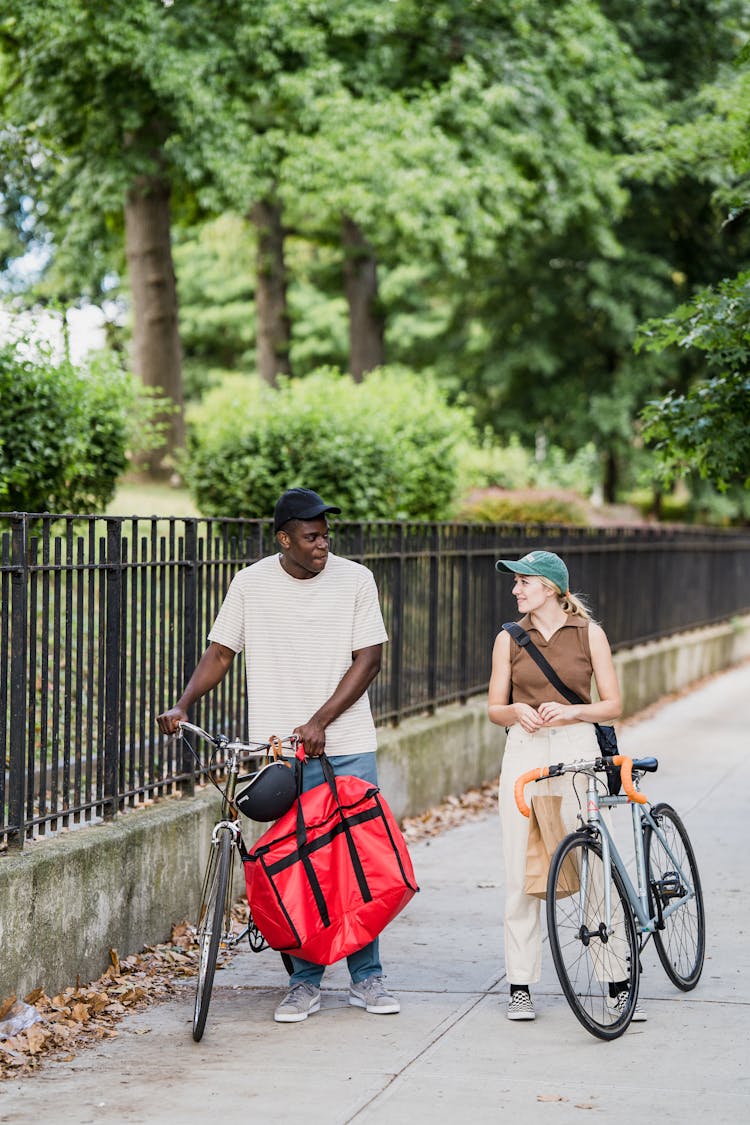 Food Delivery Man And Woman On Bicycles Carrying Food Delivery Bags Talking 