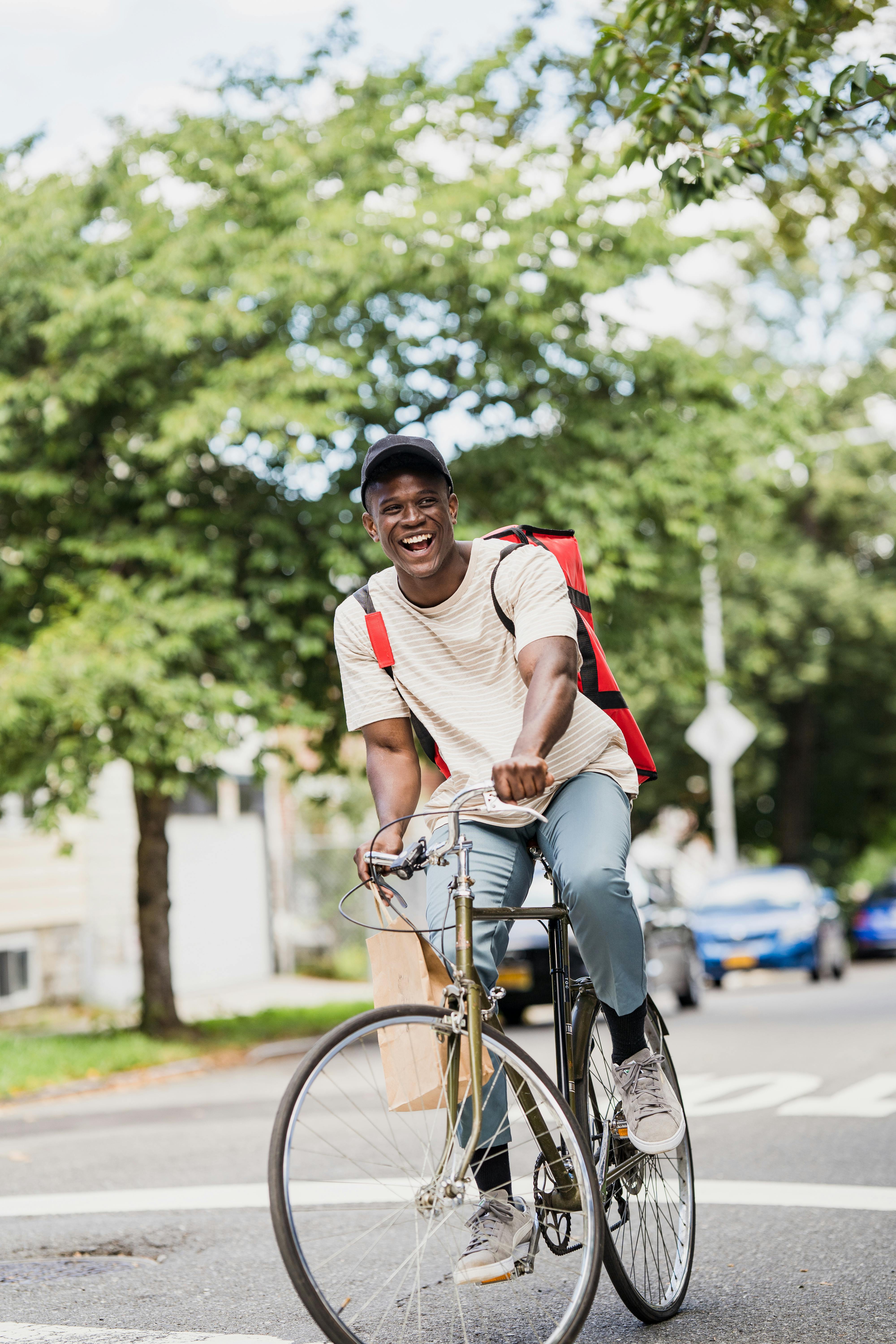 Smiling Courier with Backpack Riding Bike · Free Stock Photo